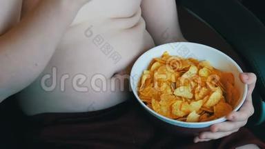 肥胖的少年身体上有着肥胖的褶皱，正在用手吃薯片.. 不健康食品，快餐.. 儿童`